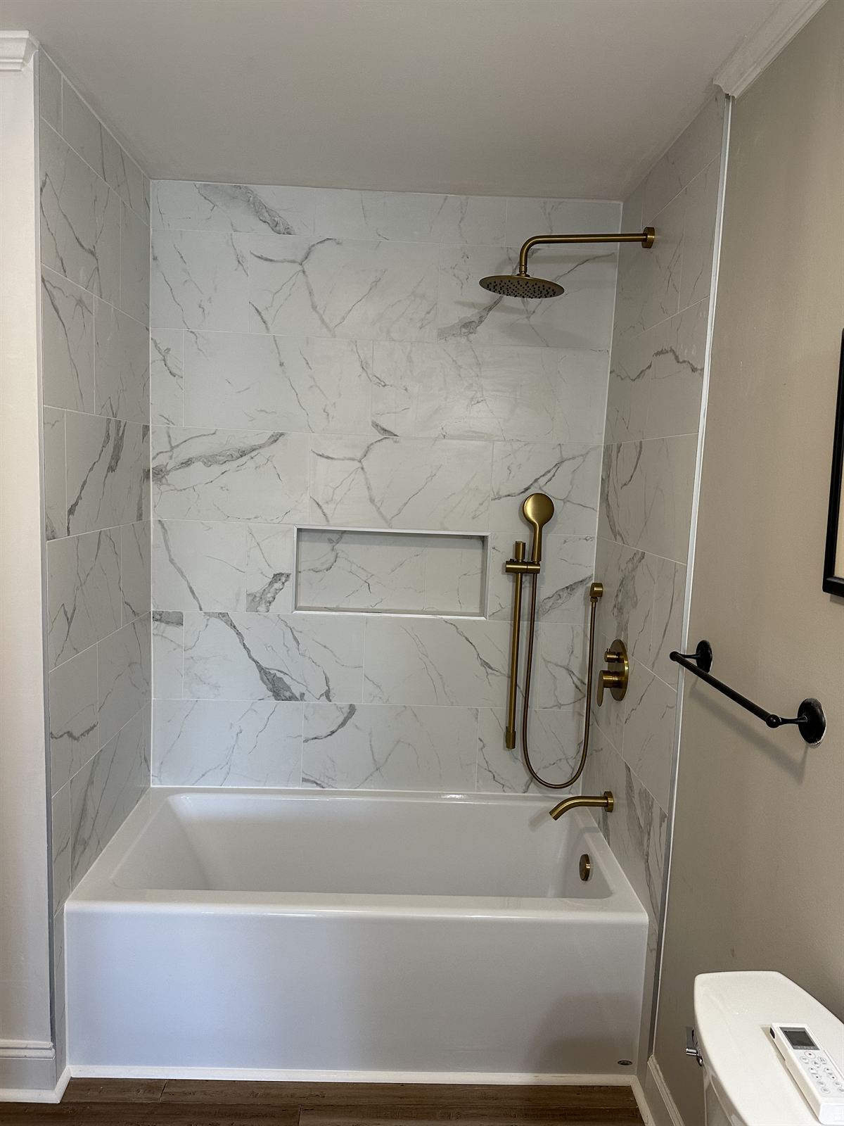 Bathroom remodel with marble-look tile tub surround, brass rain shower fixtures and tiled storage niche