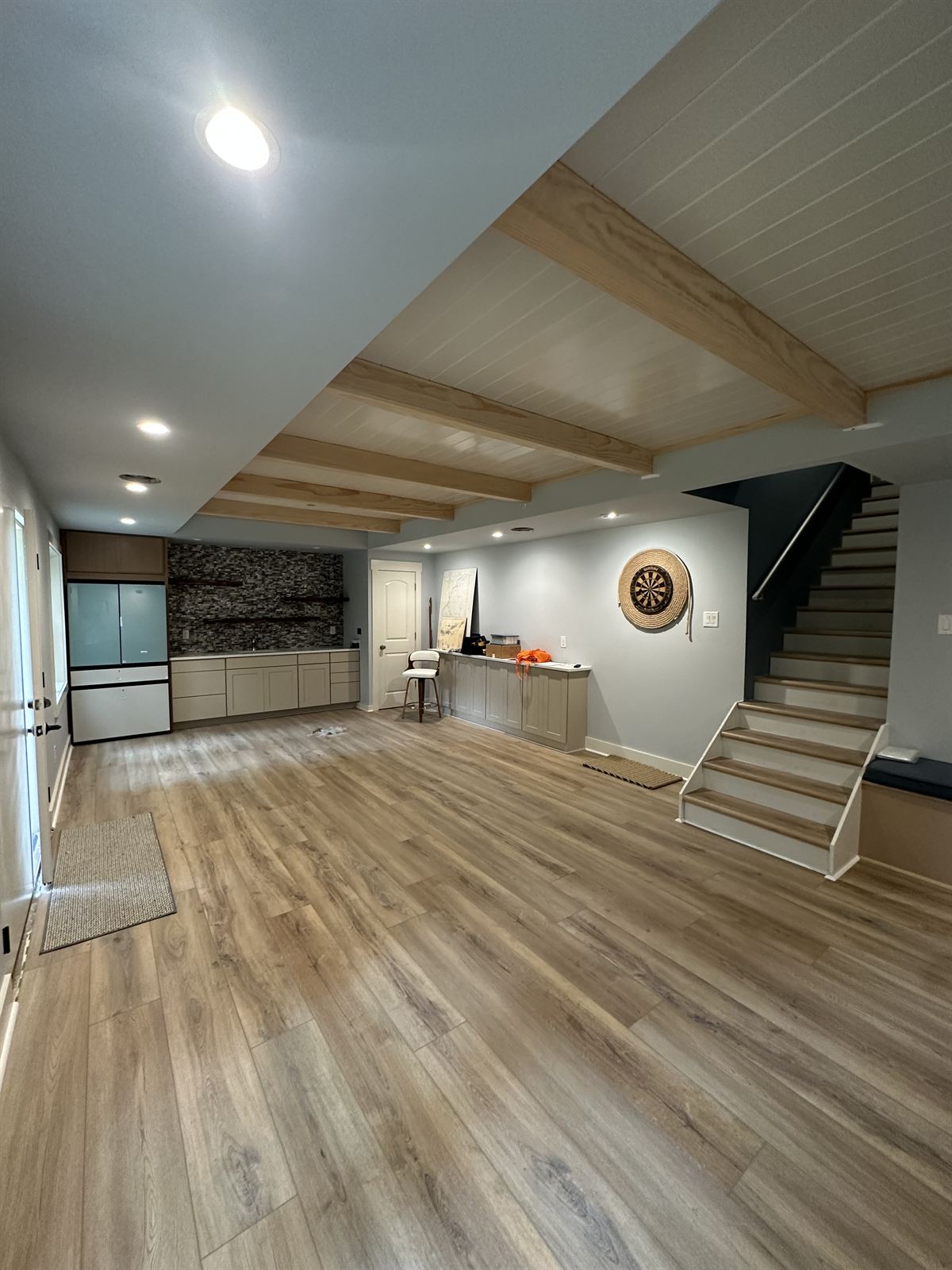 Finished basement remodel with luxury vinyl plank flooring, exposed wood beam ceiling and wet bar