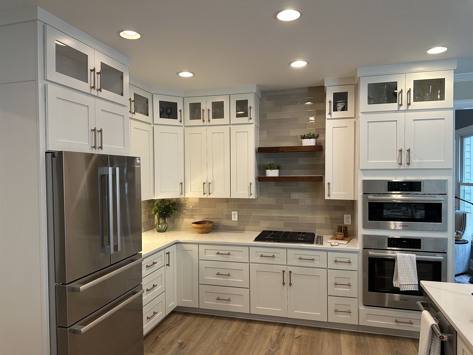 White kitchen remodel with glass-front upper cabinets, floating wood shelves and double wall ovens