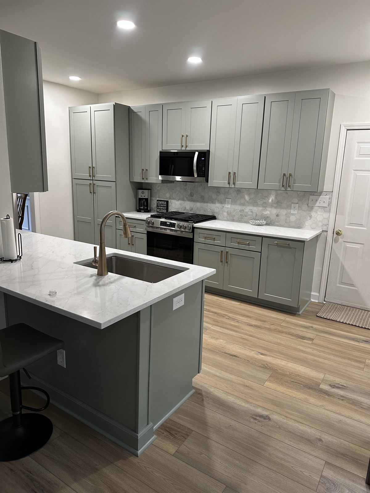 Sage green kitchen remodel with shaker cabinets, marble hexagon backsplash and luxury vinyl plank flooring