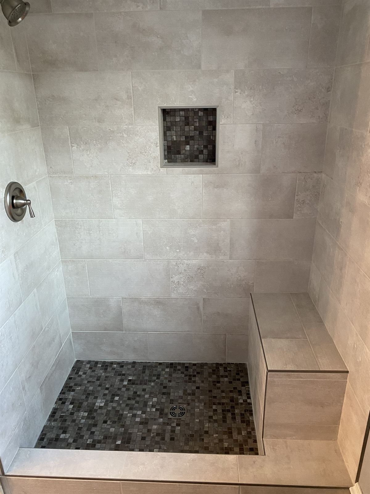Walk-in tile shower from a bathroom remodel with mosaic floor, built-in bench and storage niche