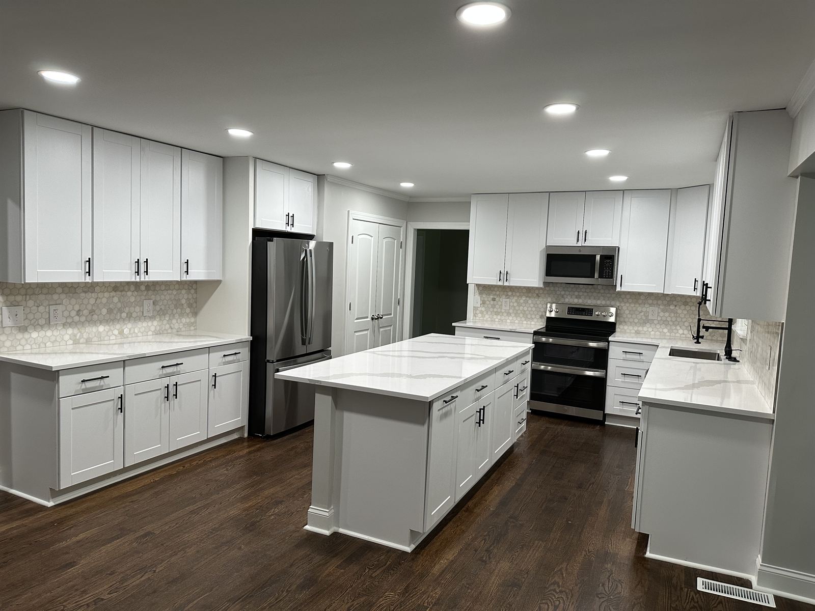 White shaker kitchen remodel with quartz island, black hardware and hardwood floors